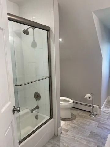 A modern bathroom featuring a glass-enclosed shower, a white toilet, and light-colored wood-look flooring.