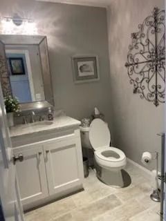 A modern bathroom with grey walls, a white vanity with a mirror above, a white toilet, and a metal wall-mounted decoration.