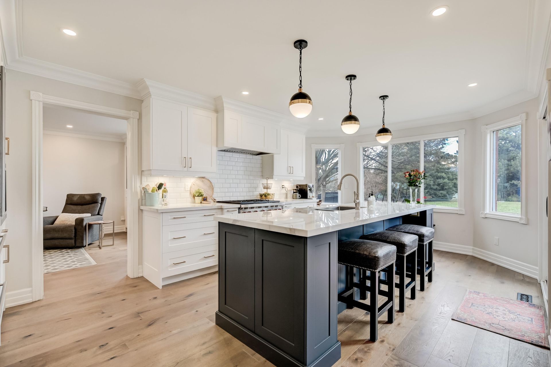 A bright, modern kitchen features white cabinetry, a dark gray island with stools, and light wood floors.