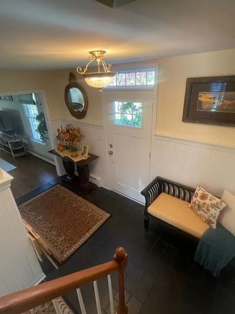 An entry hallway with dark floors, a white door, a mirror, an area rug, and a bench with a patterned cushion.