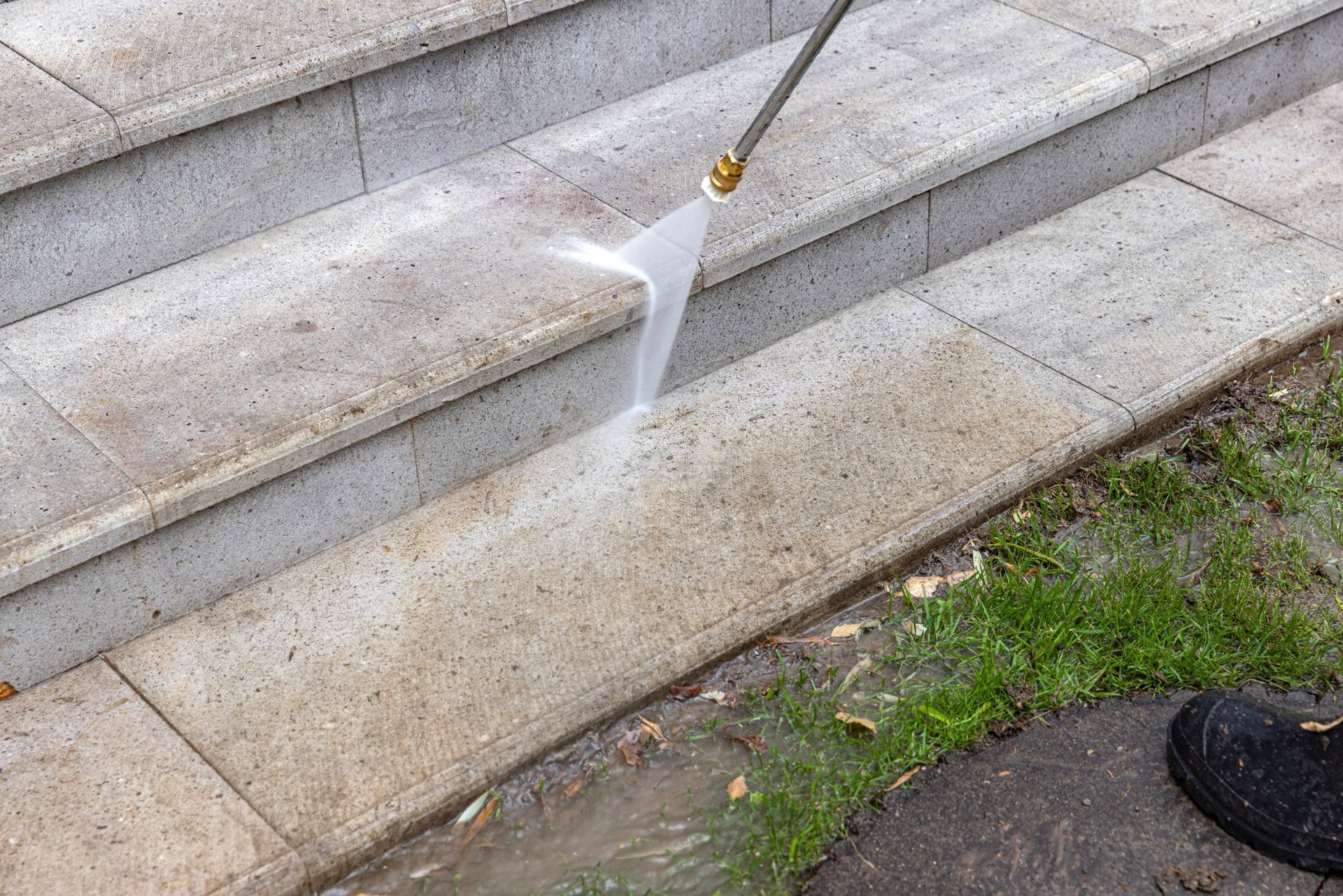 A person uses a pressure washer to clean dirty stone outdoor steps.