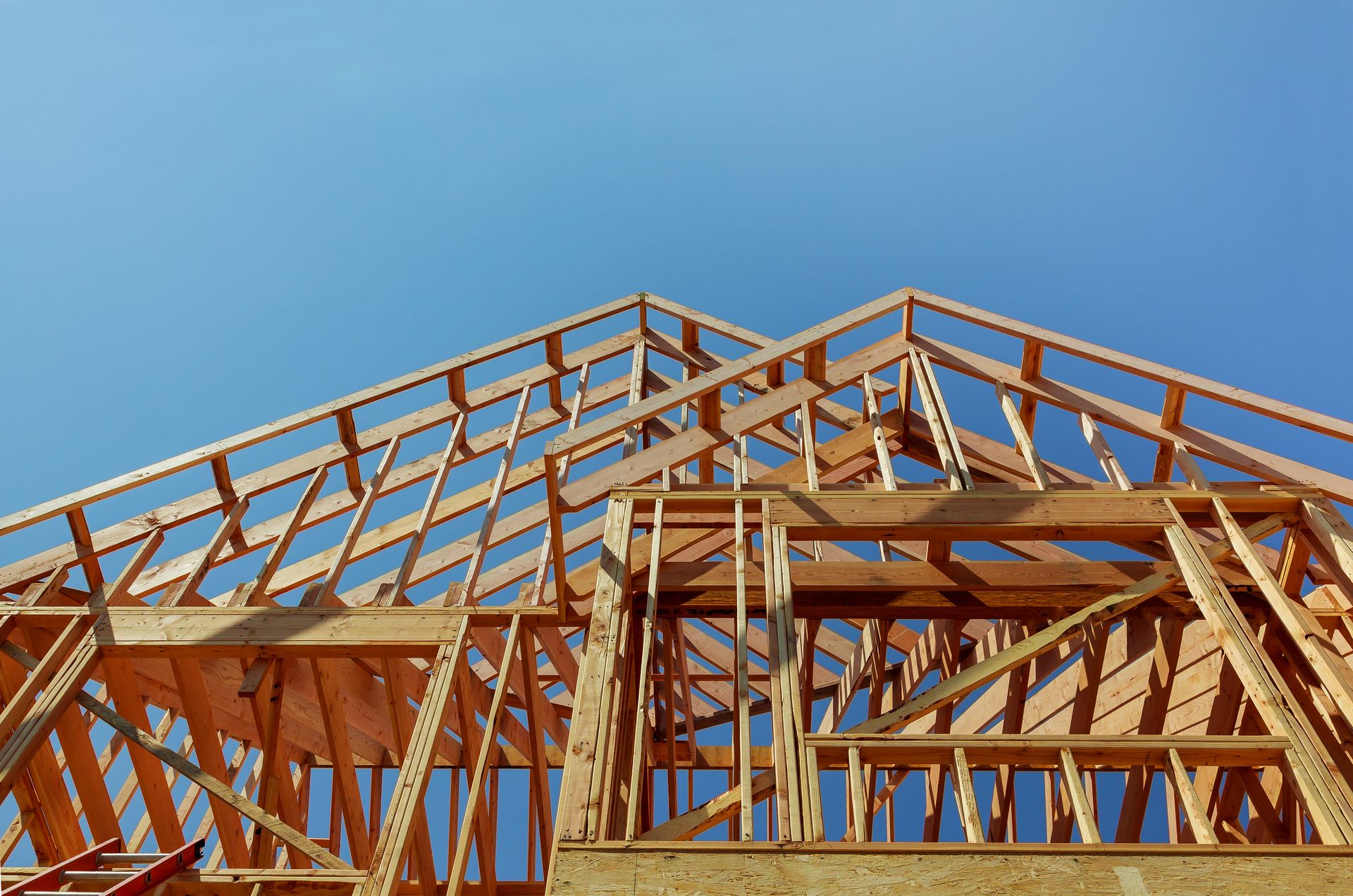 A low-angle view of the wooden frame of a house under construction against a clear blue sky.