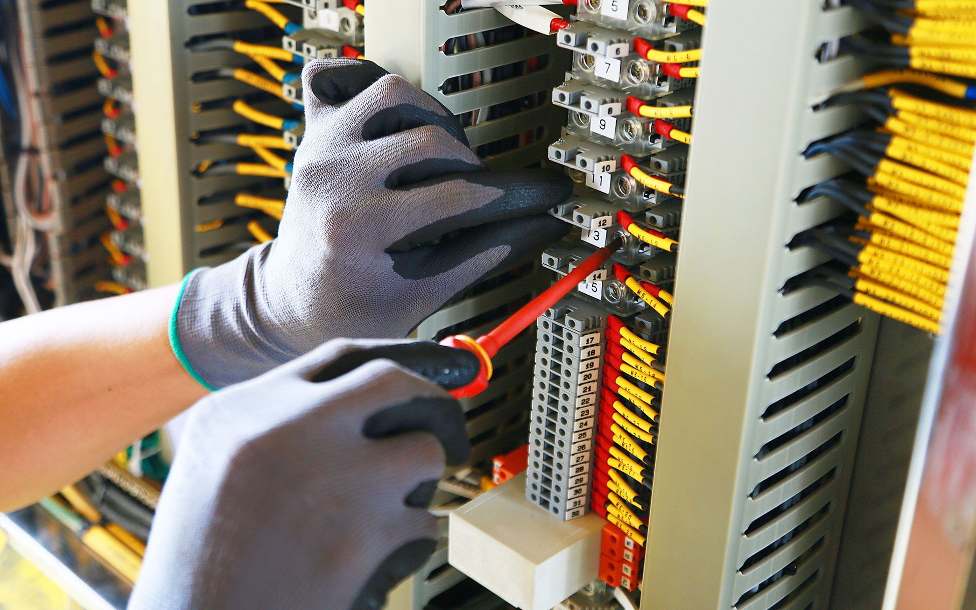 A person is working on an electrical box with a wrench.