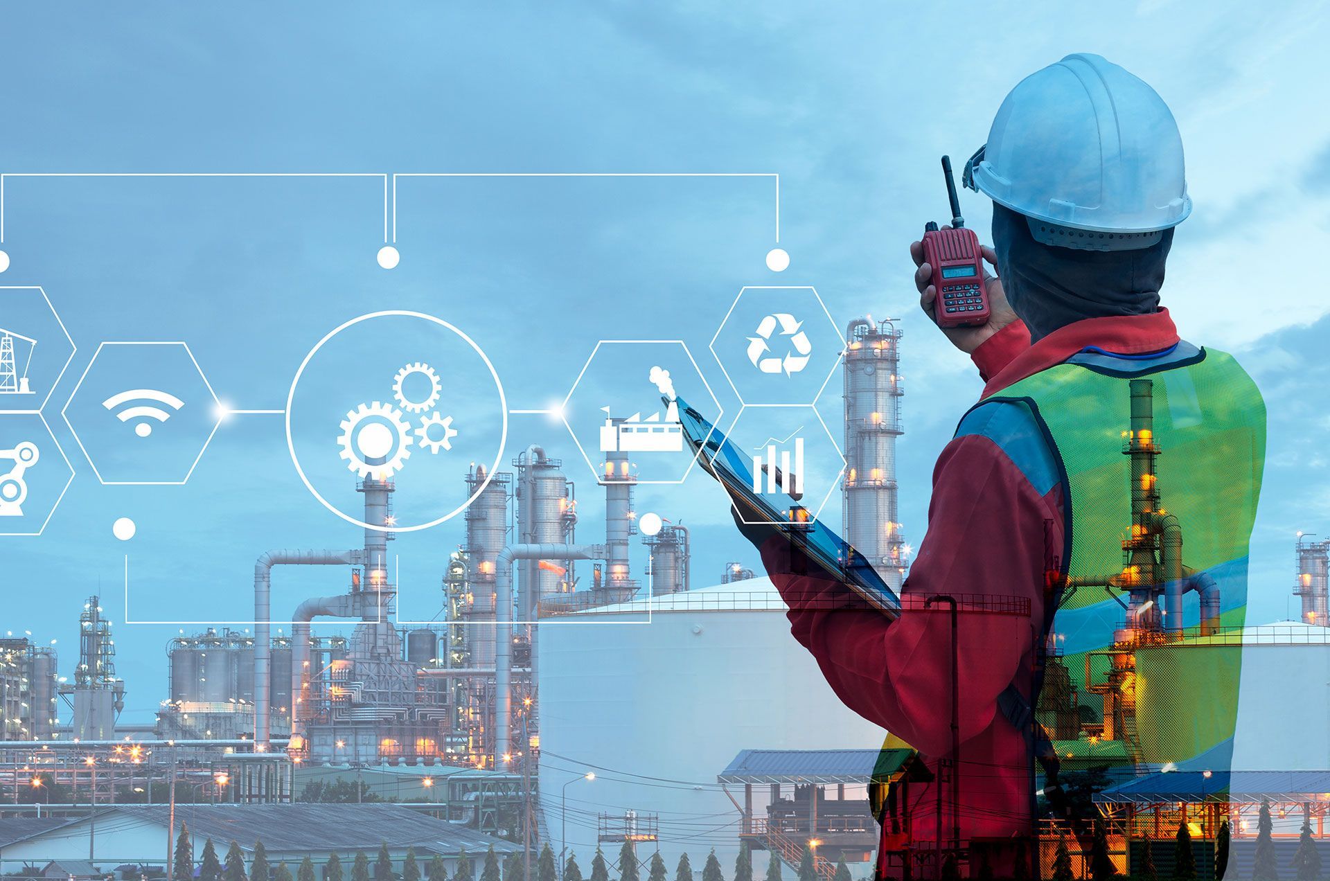 A man is standing in front of a factory holding a tablet and a walkie talkie.
