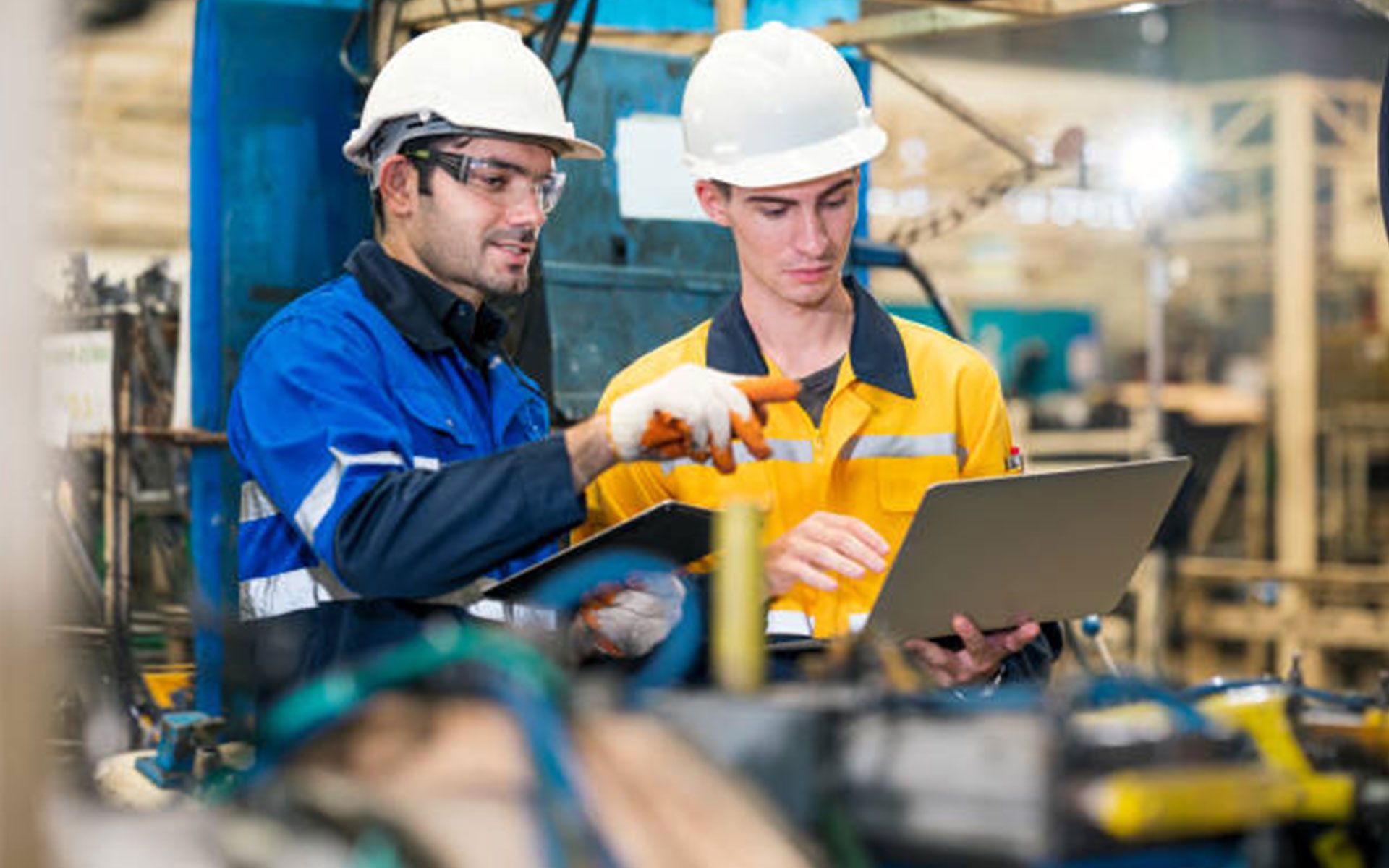Two men are working in a factory and looking at a laptop.