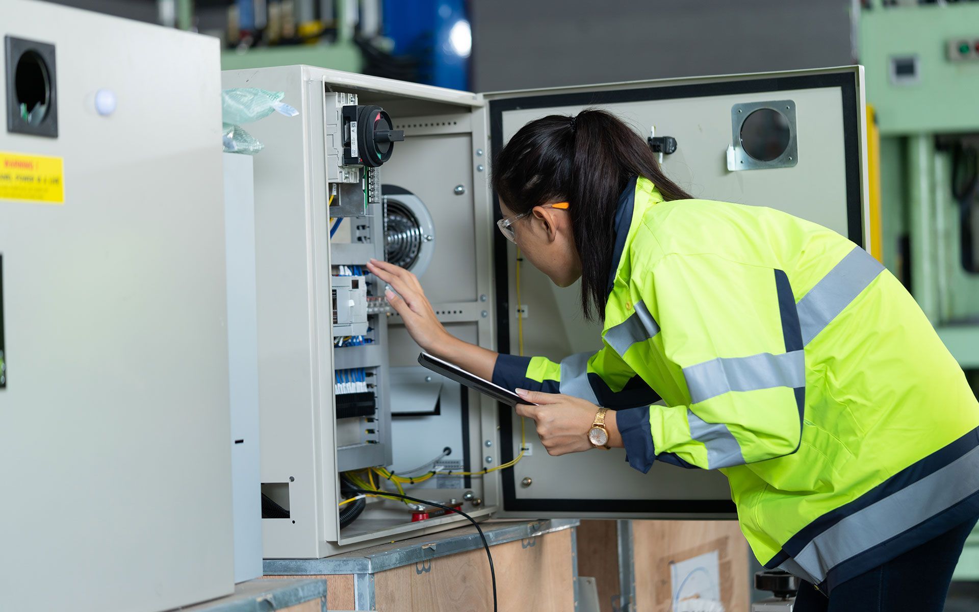 A woman is working on an electrical box in a factory.