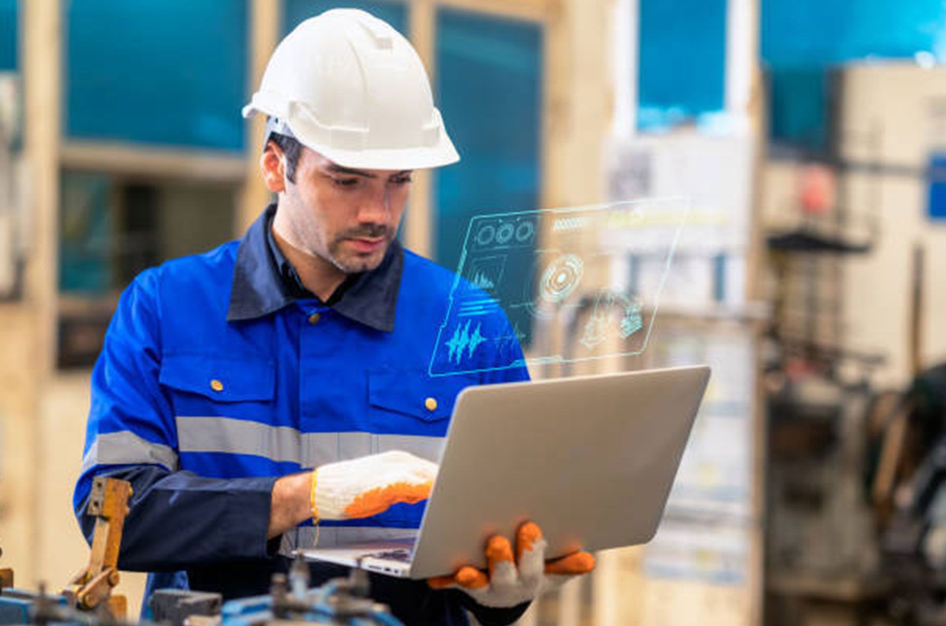 A man in a hard hat is using a laptop computer in a factory.