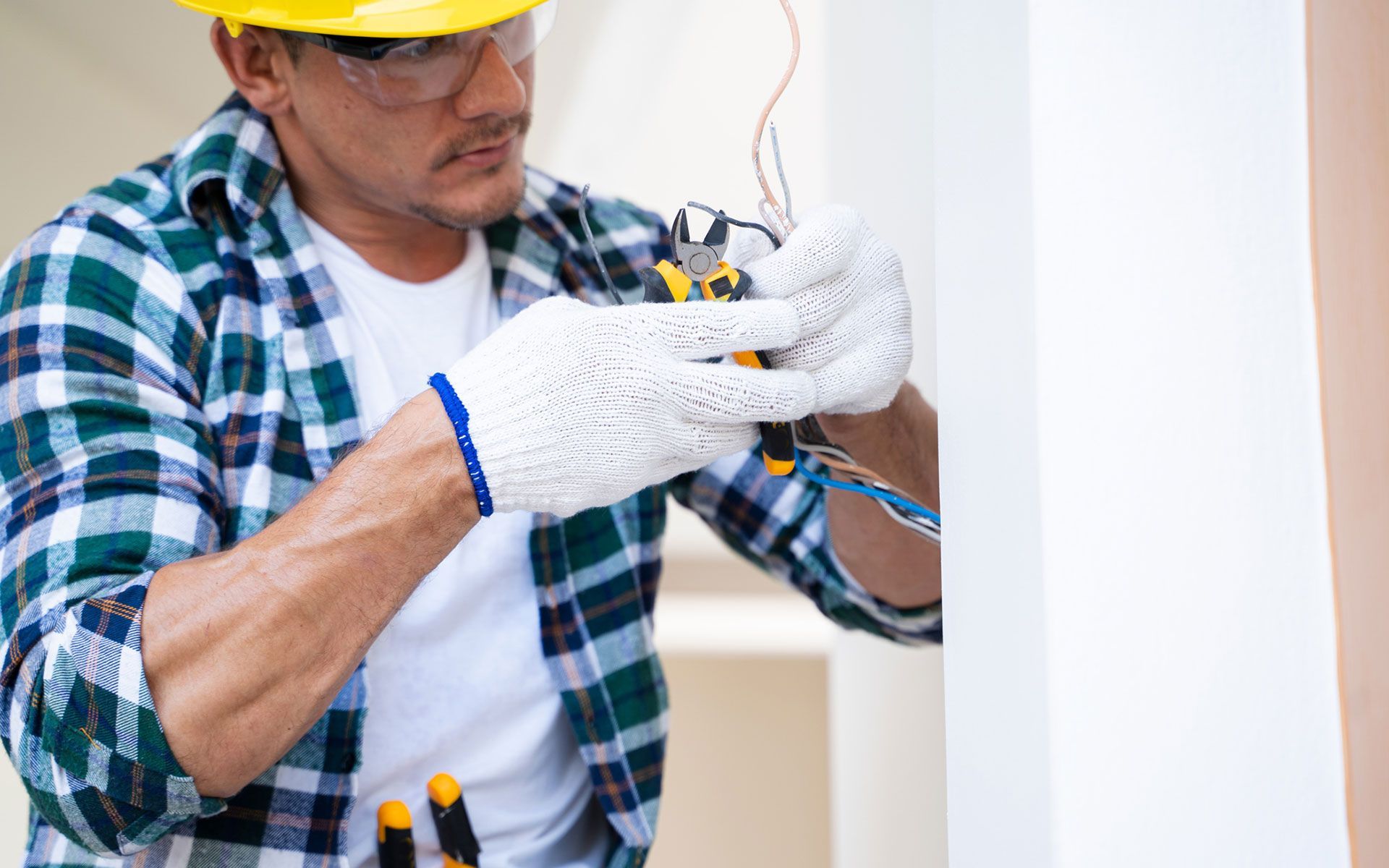 A man wearing a hard hat and safety glasses is working on a wall.