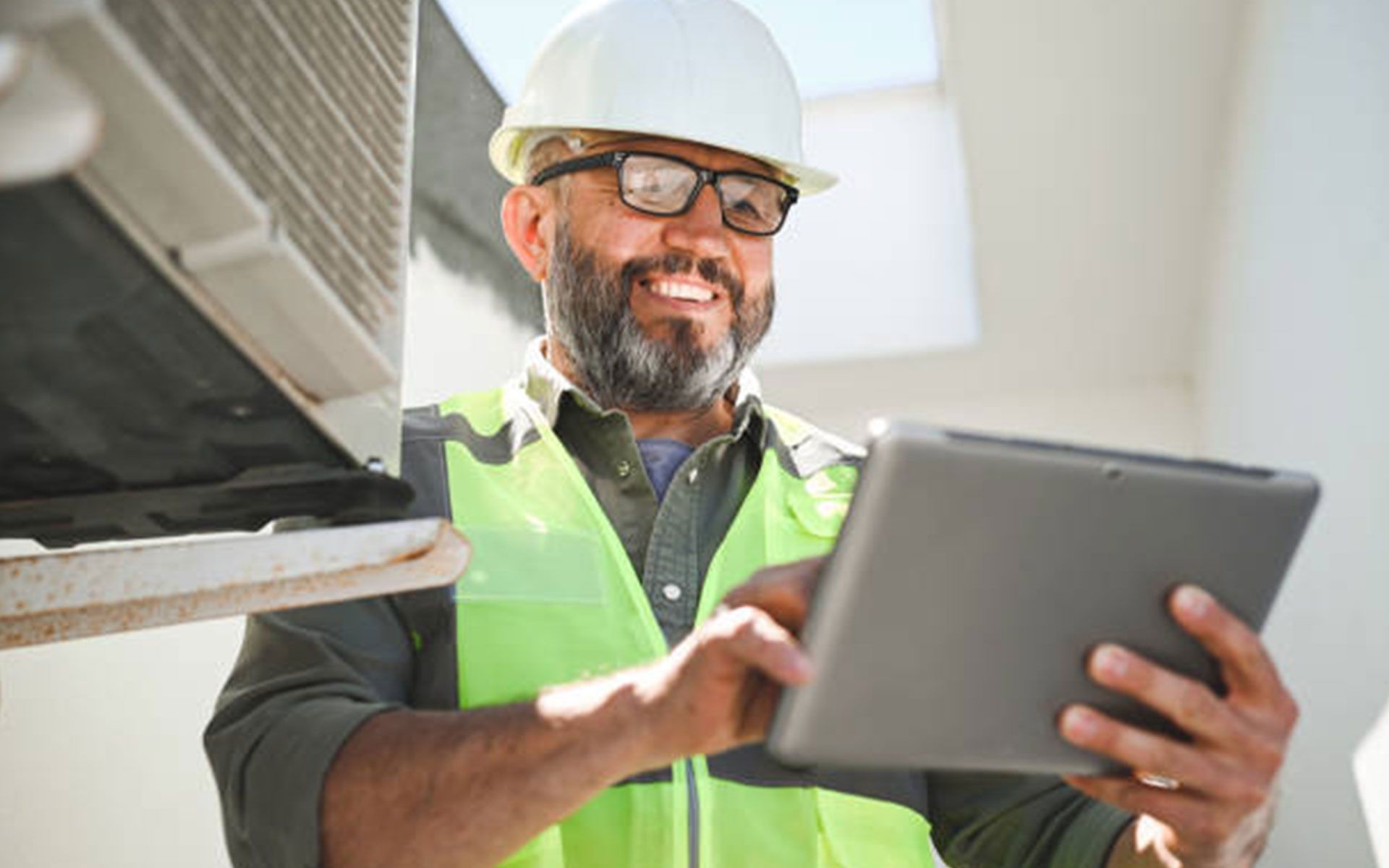 A man wearing a hard hat and safety vest is holding a tablet computer.