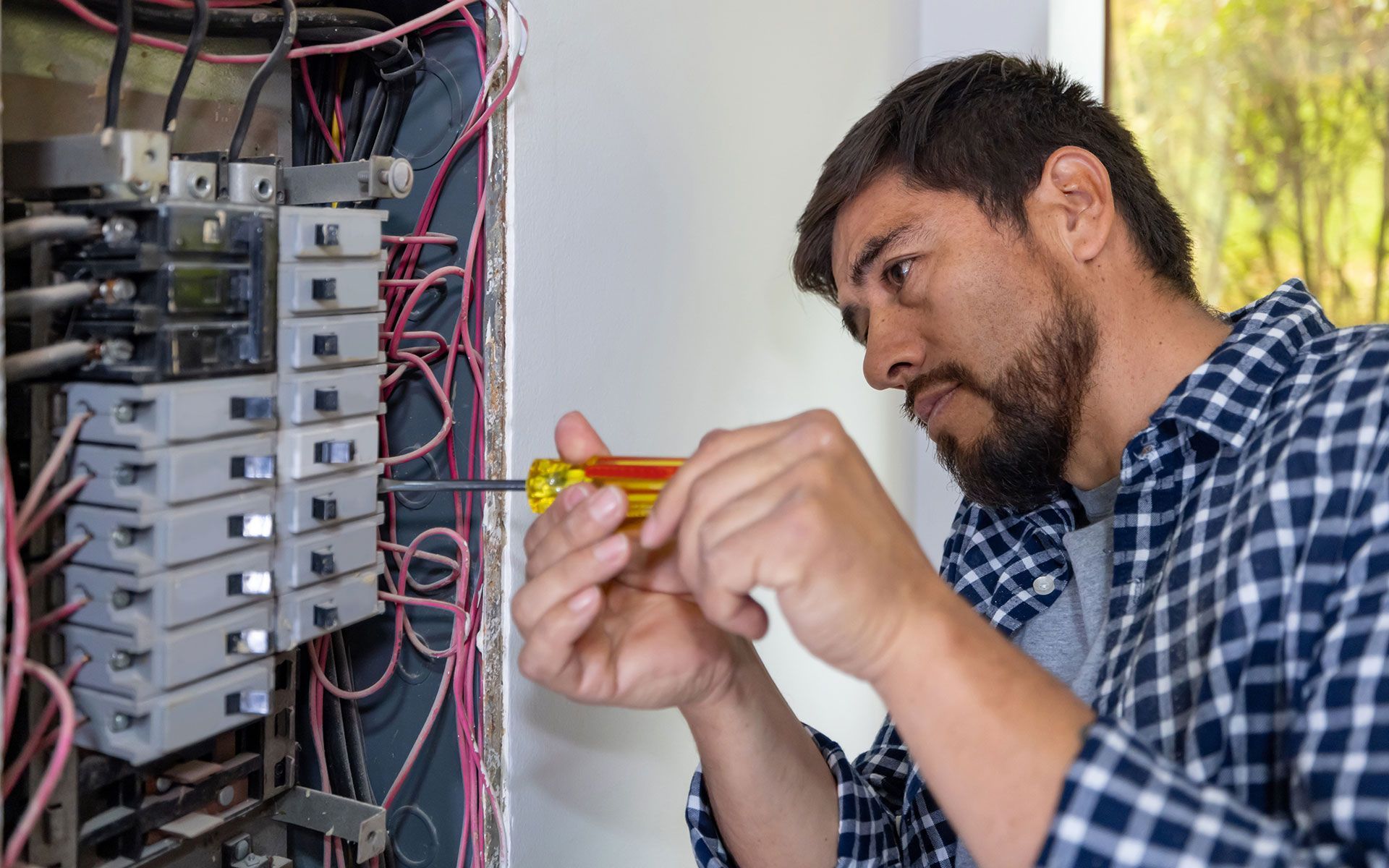 A man is working on an electrical box with a screwdriver.