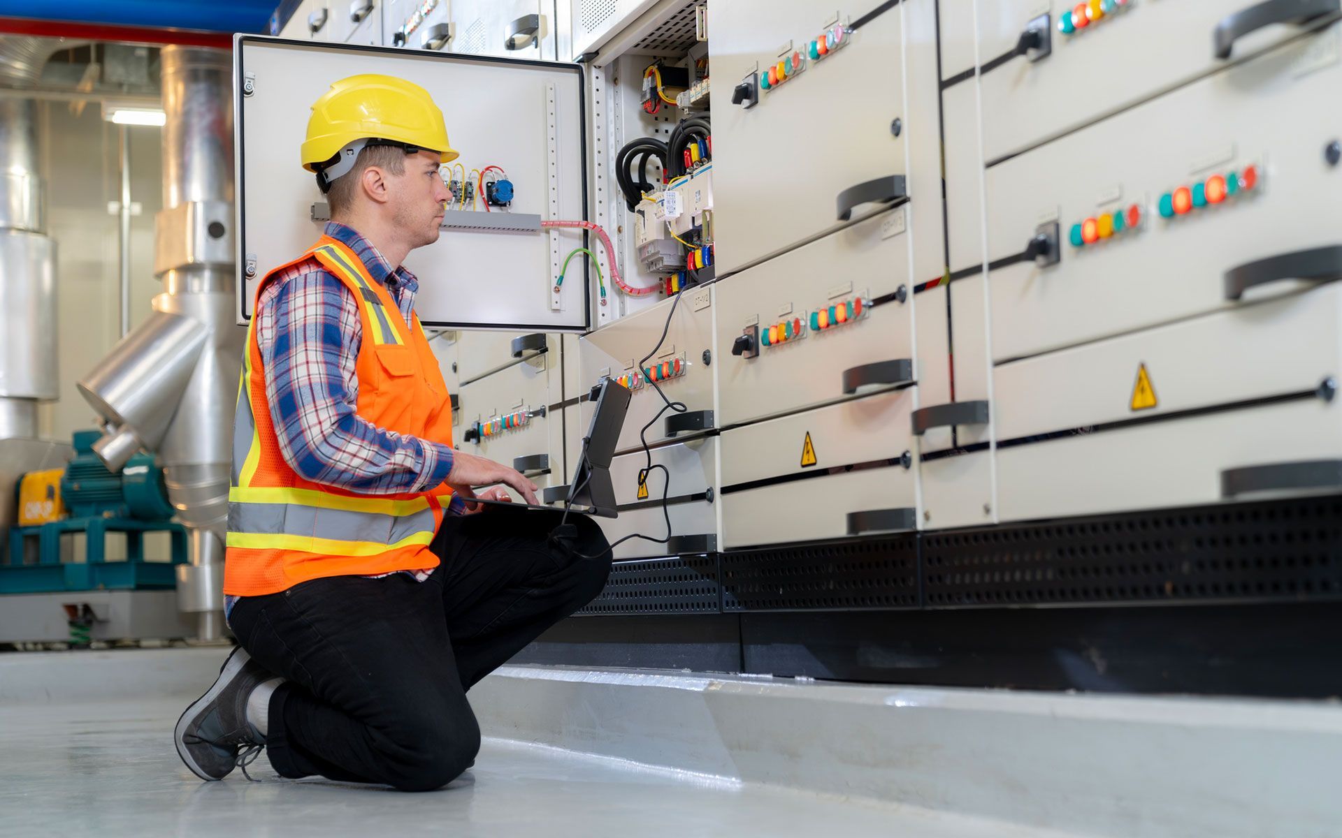 A man is kneeling down in front of a wall while using a laptop computer.