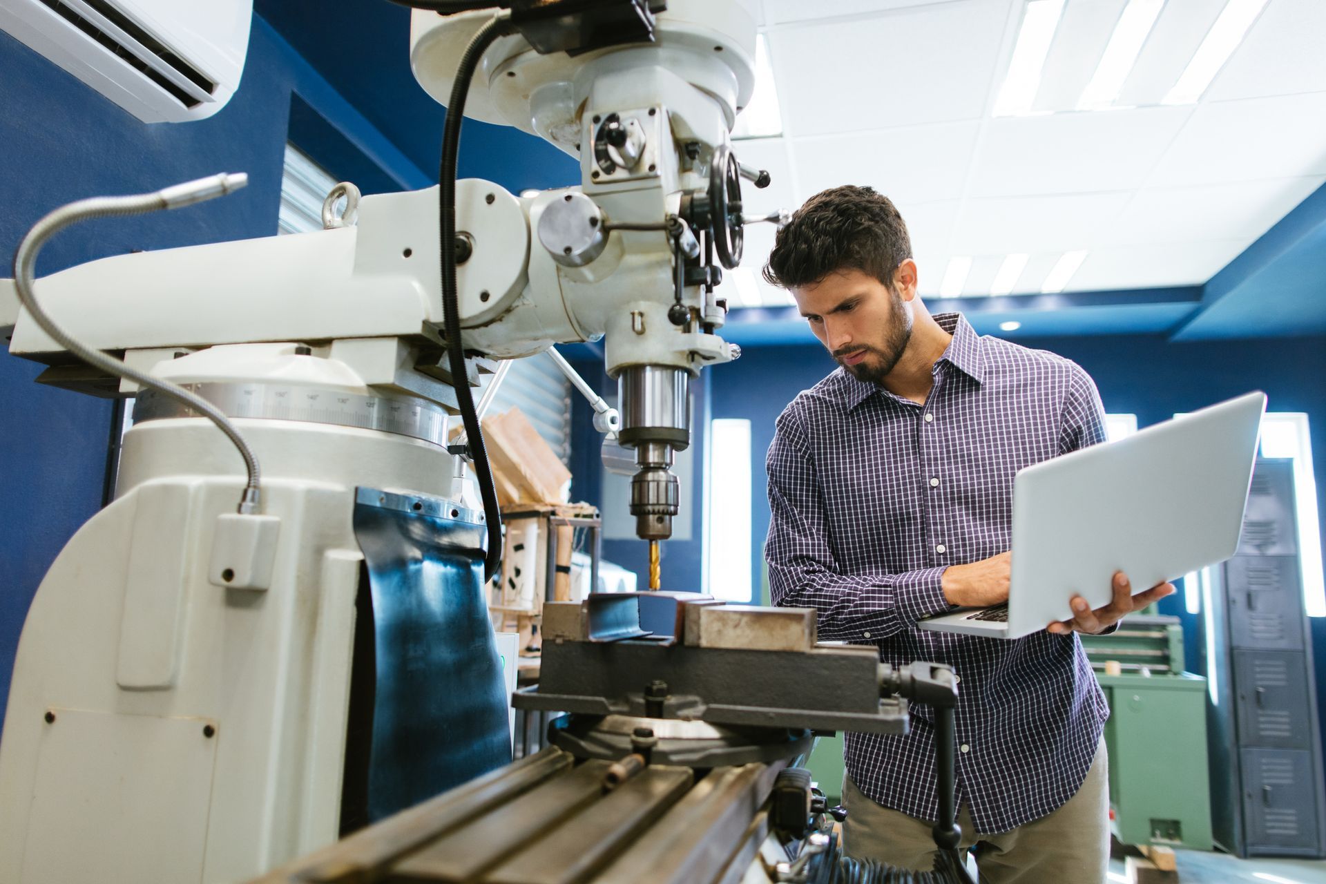 A man is working on a machine while holding a laptop.