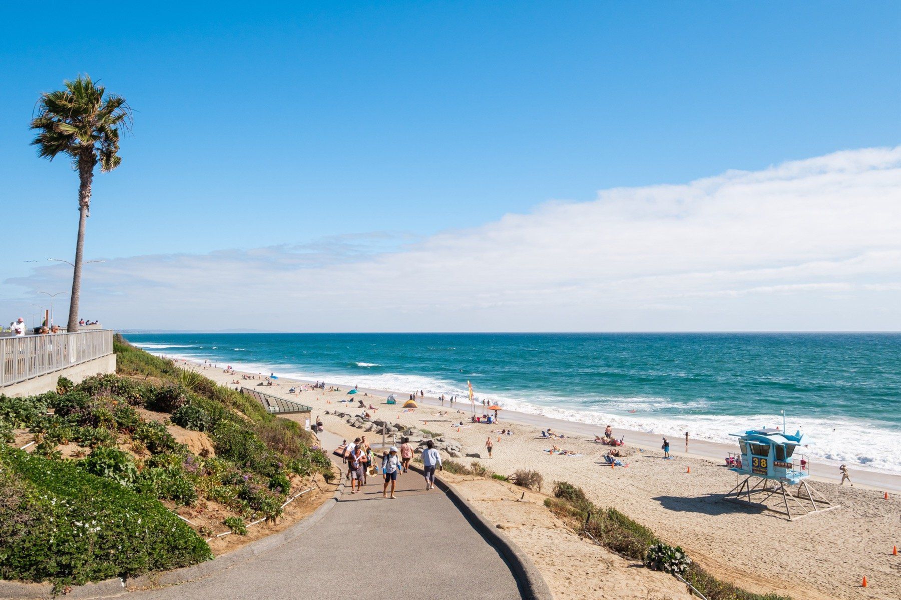 A group of people are walking down a path to the beach.
