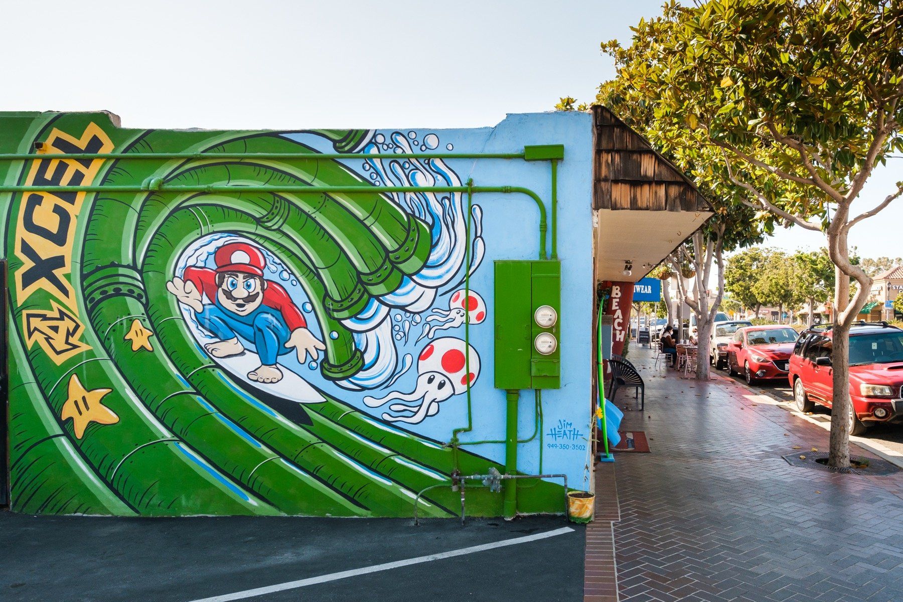 A mural of mario on a surfboard is on the side of a building.