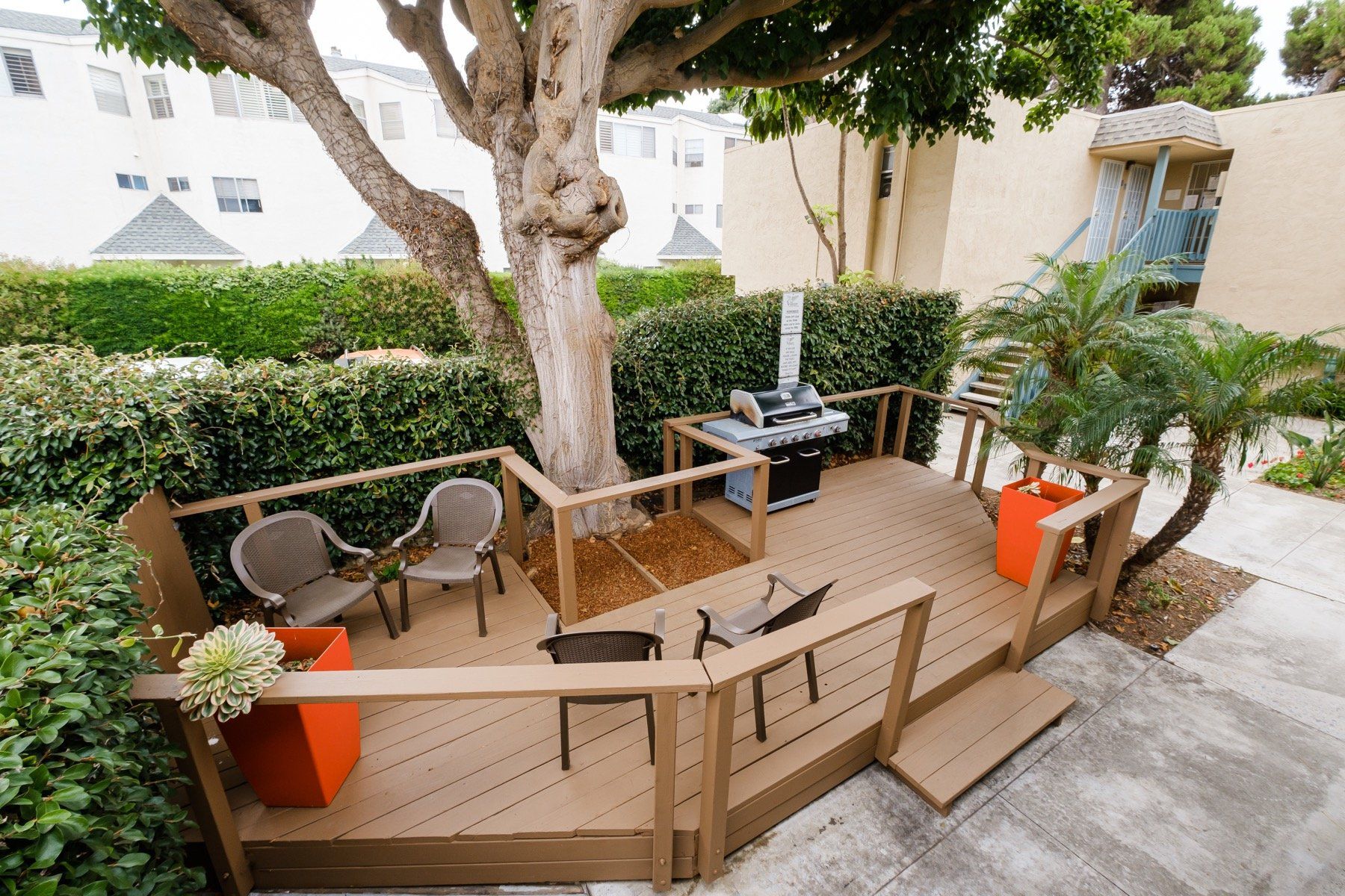 A wooden deck with chairs and a grill under a tree