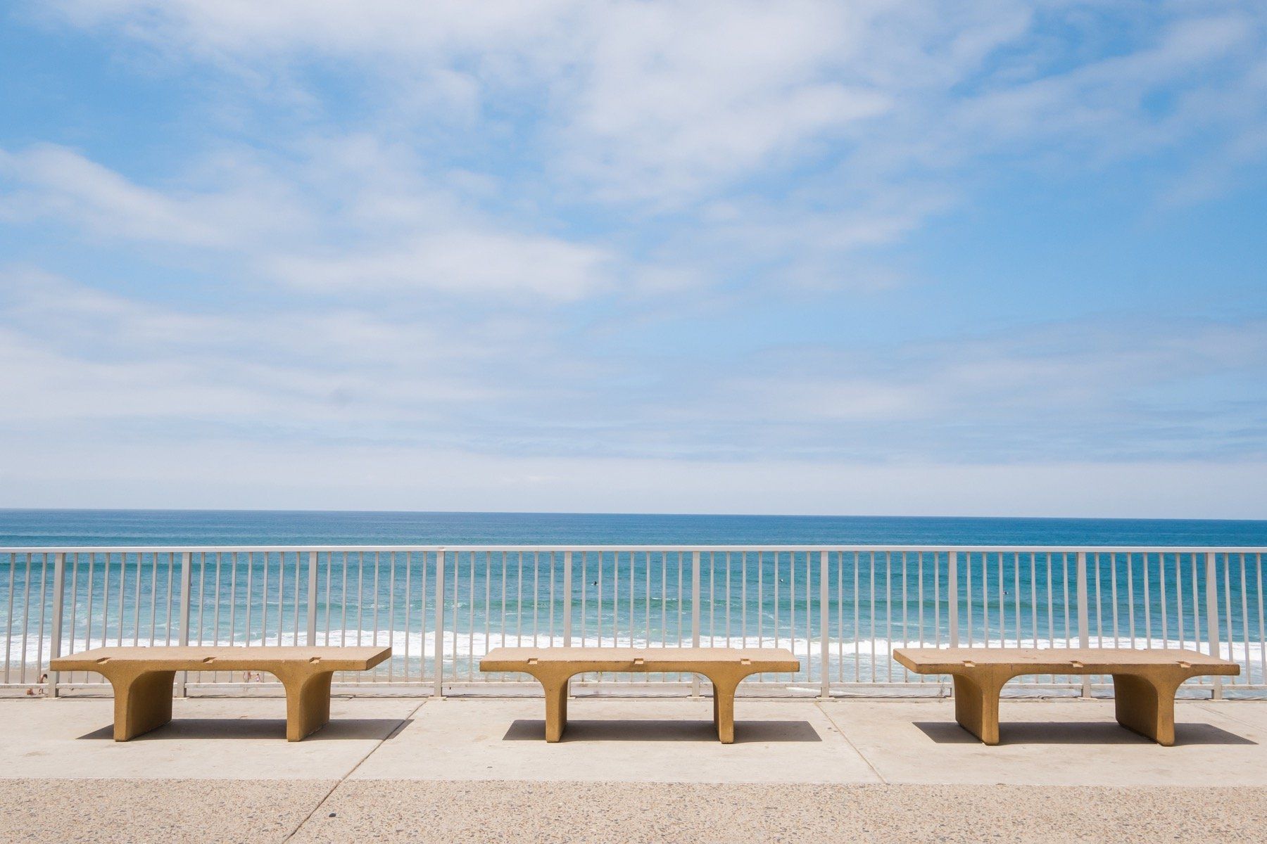 Three benches are lined up on a sidewalk overlooking the ocean.