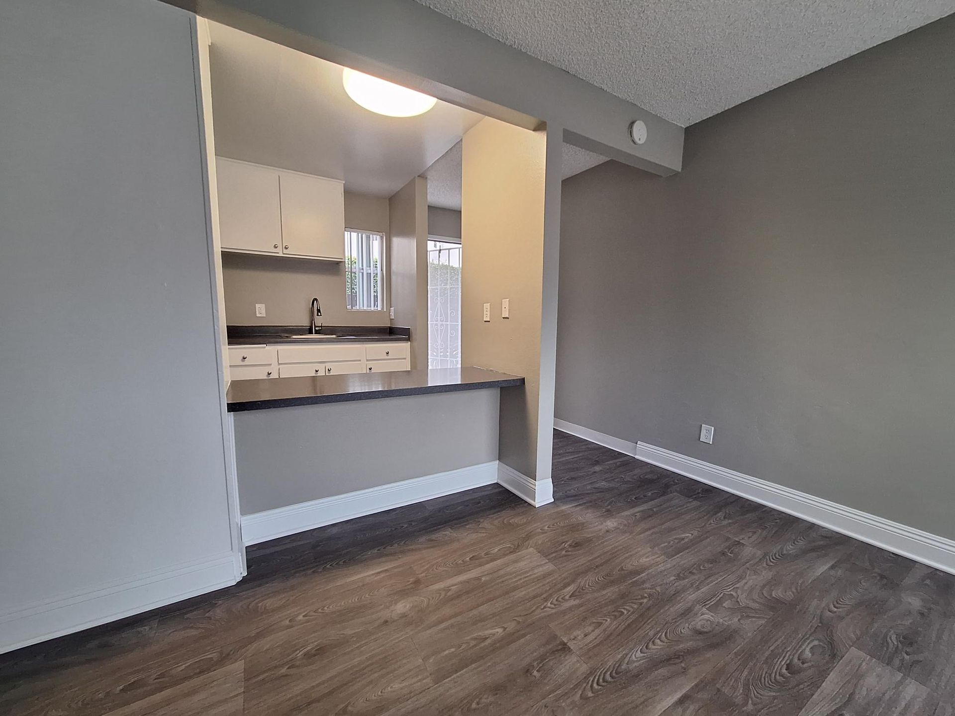 A living room with hardwood floors and a kitchen in the background.