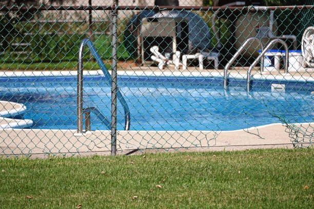 A chain-link fence surrounds a blue swimming pool with metal handrails.