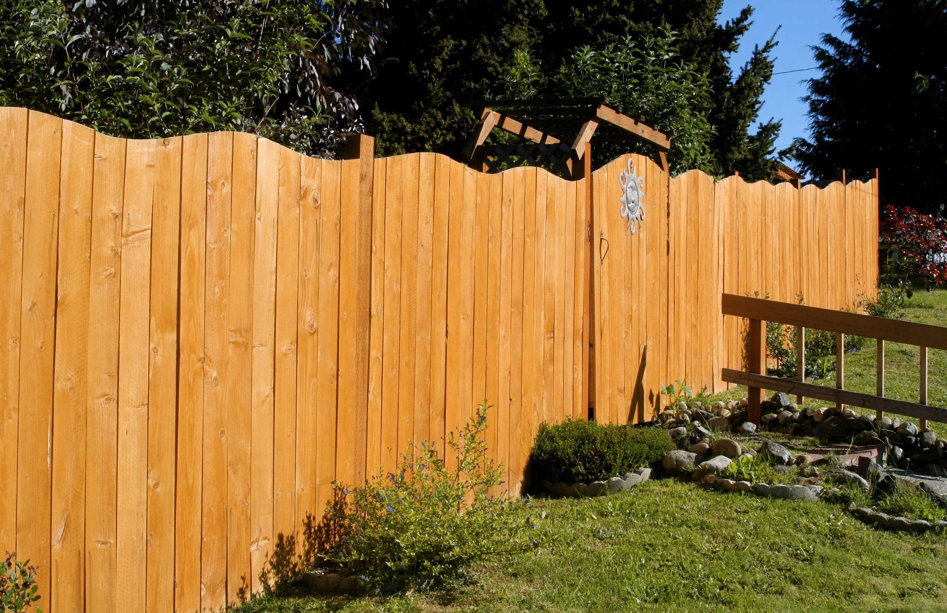 Wooden fence with a gate, stained orange, borders a green lawn and garden.