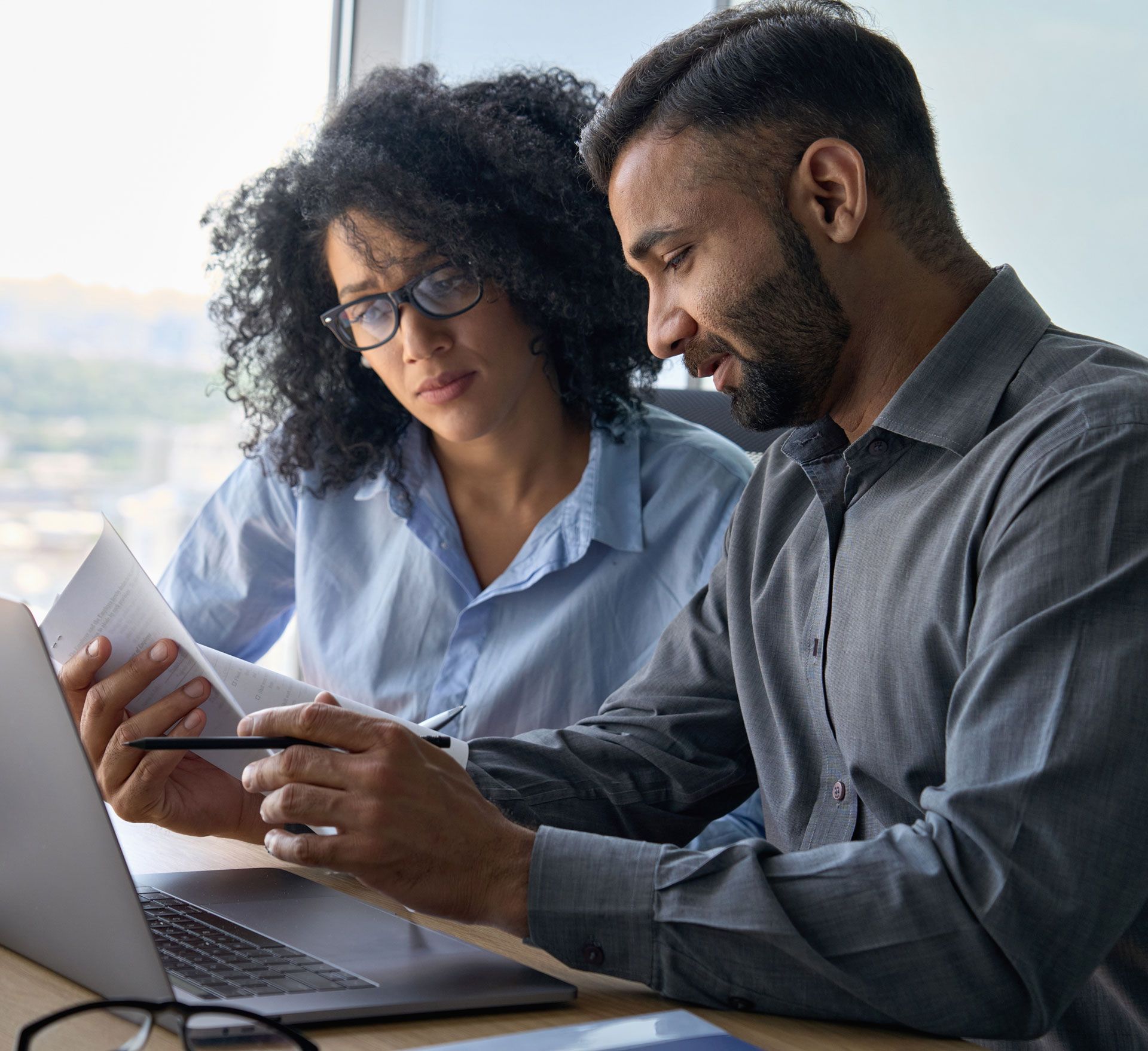 A man and a woman are sitting at a table looking at a laptop.