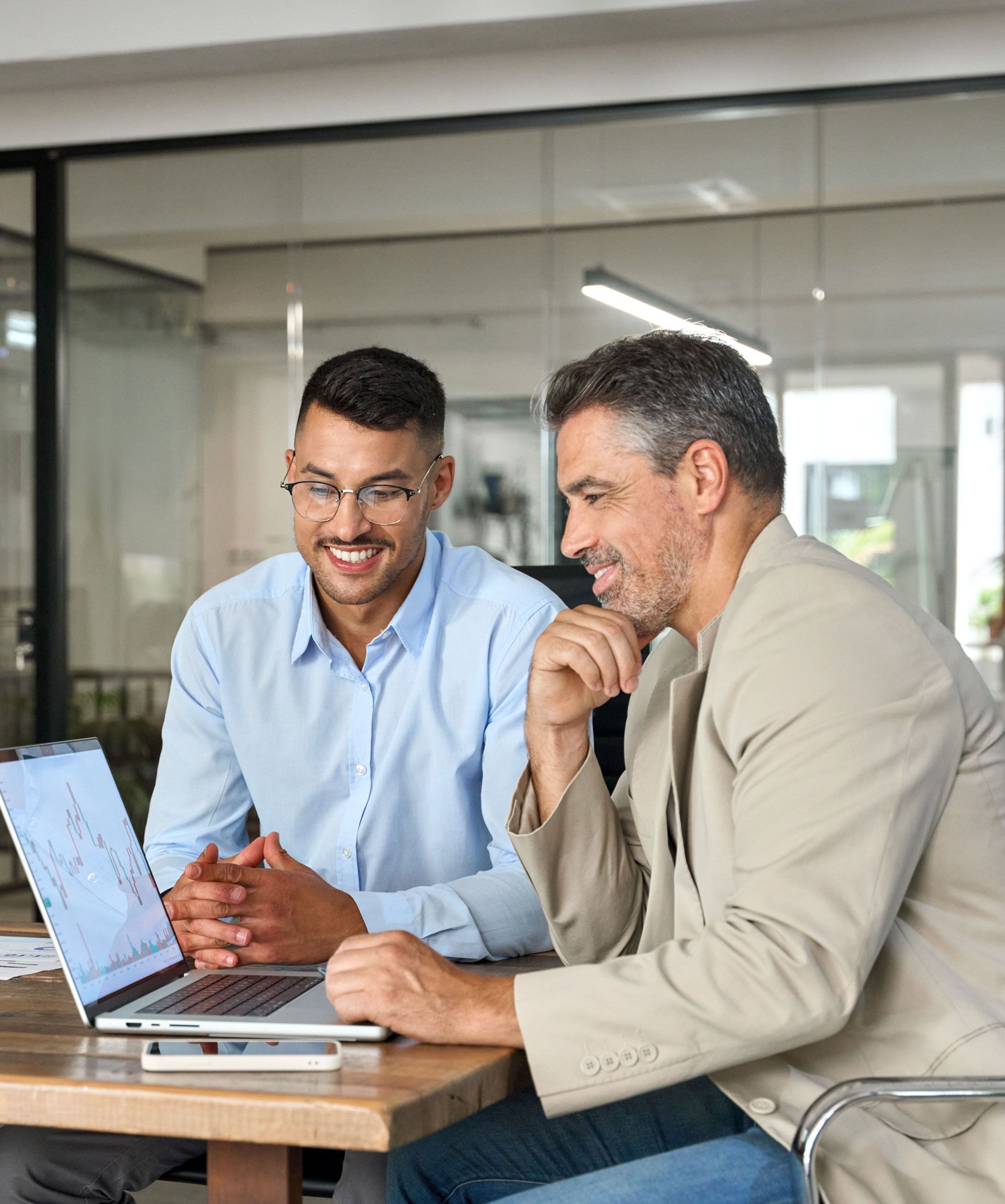 Two men are sitting at a table looking at a laptop.