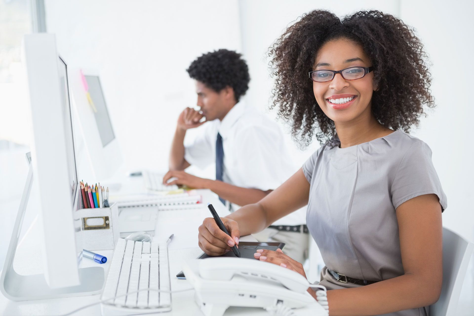 A woman is smiling while sitting at a desk in front of a computer.