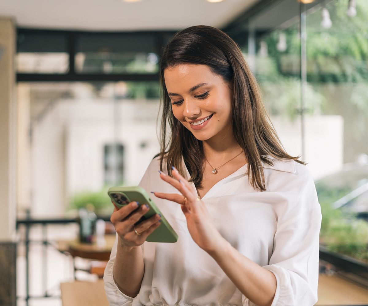 A woman is smiling while looking at her cell phone.