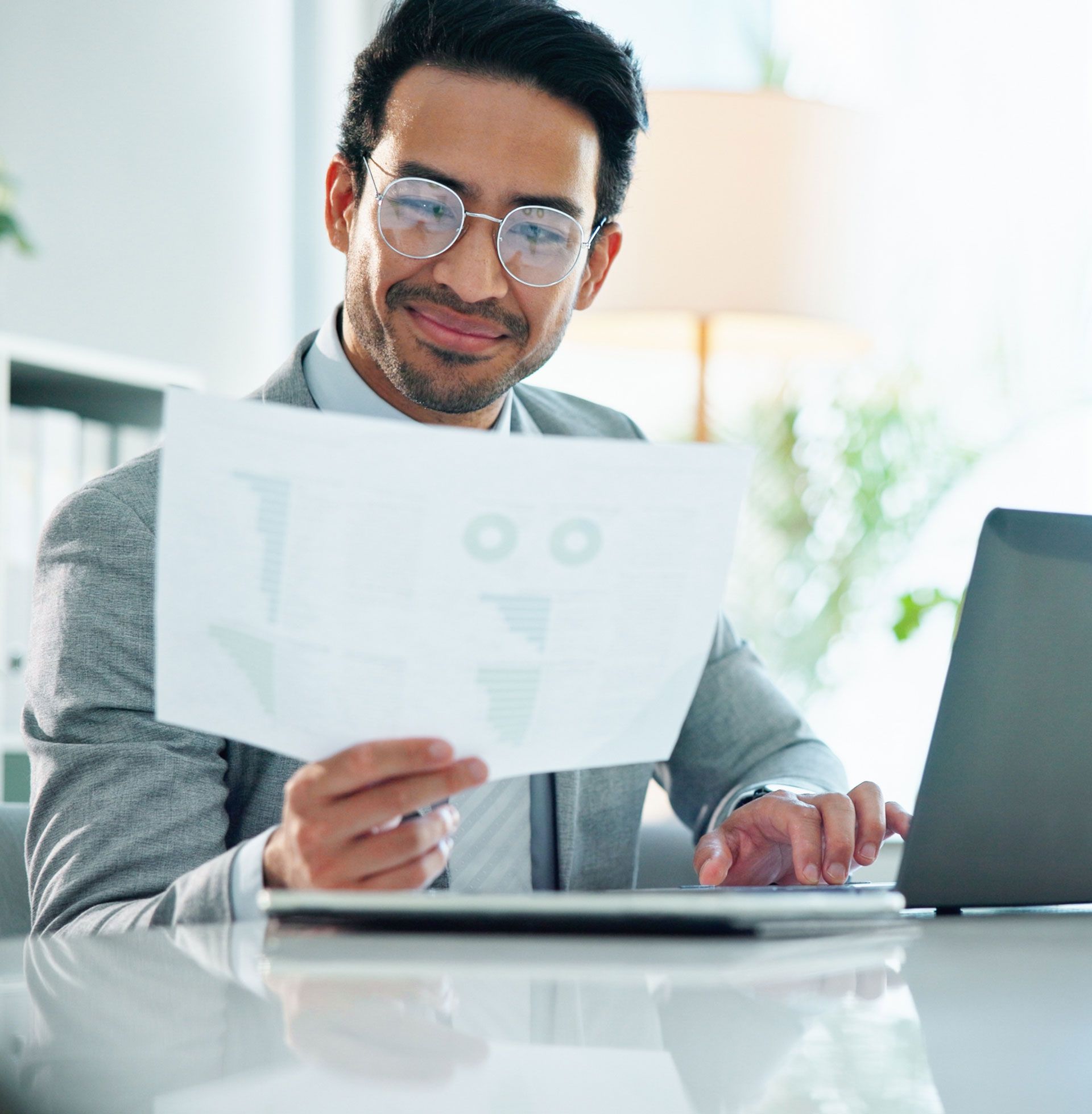 A man wearing glasses is sitting at a desk looking at a piece of paper