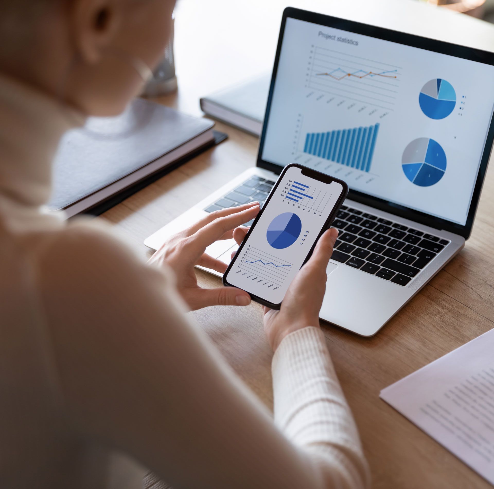 A woman is holding a cell phone in front of a laptop computer.