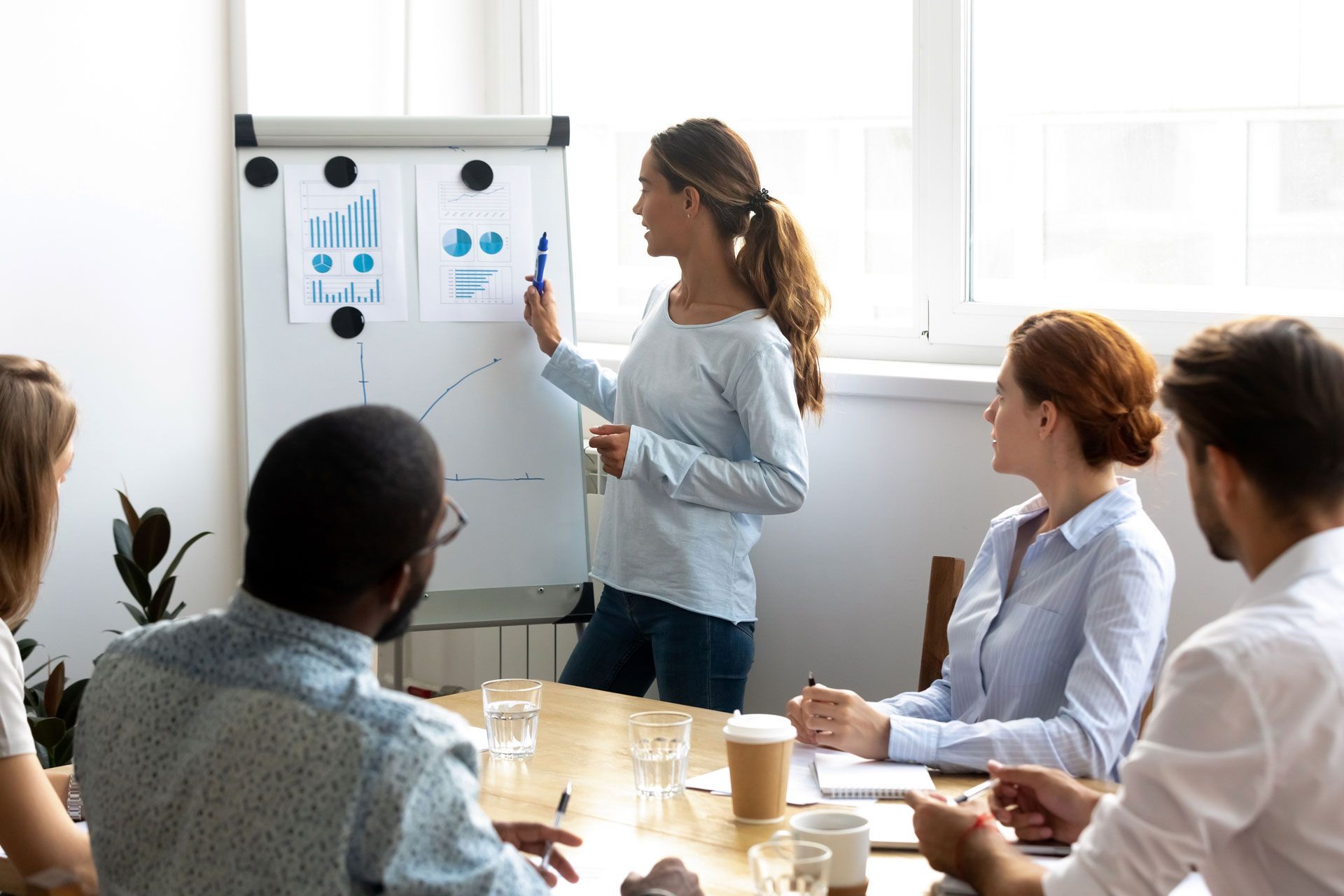 A woman is giving a presentation to a group of people sitting around a table.