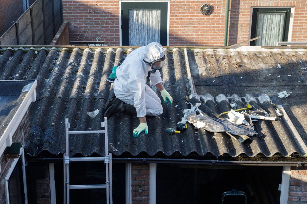 A Man in A Protective Suit Is Kneeling on Top of A Roof — Northern Rivers Demolition & Asbestos in Tweed Heads, NSW