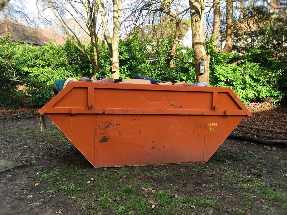 A Large Orange Dumpster Is Sitting in The Grass in A Park — Northern Rivers Demolition & Asbestos in Grafton, NSW