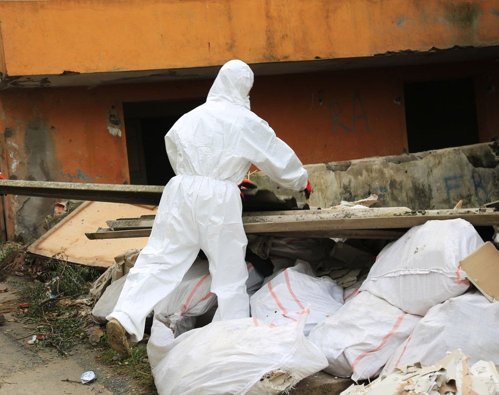 A Man in A Protective Suit Is Standing in Front of A Pile of Trash — Northern Rivers Demolition & Asbestos in Casino, NSW