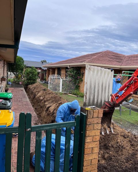 A Man in A Blue Suit Is Digging a Hole in Front of A House — Northern Rivers Demolition & Asbestos in Skennars Head, NSW