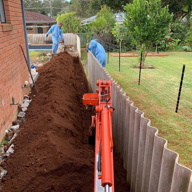 An Excavator Is Digging Trench in The Ground Next to A Fence — Northern Rivers Demolition & Asbestos in Yamba, NSW