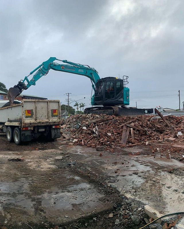 A Large Excavator Is Loading a Dump Truck with Bricks — Northern Rivers Demolition & Asbestos in Byron Bay, NSW