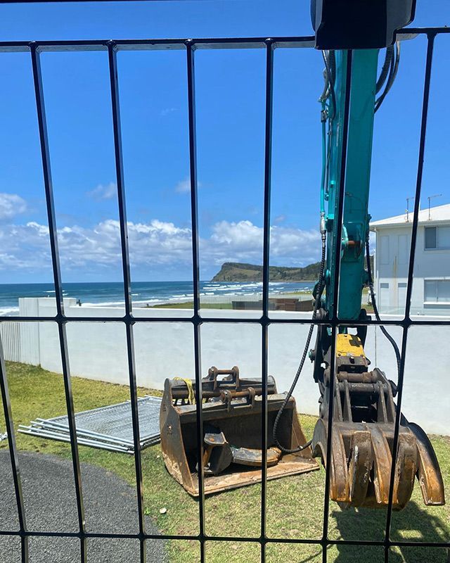 An Excavator Is Behind a Fence with A View of The Ocean — Northern Rivers Demolition & Asbestos in Lismore, NSW