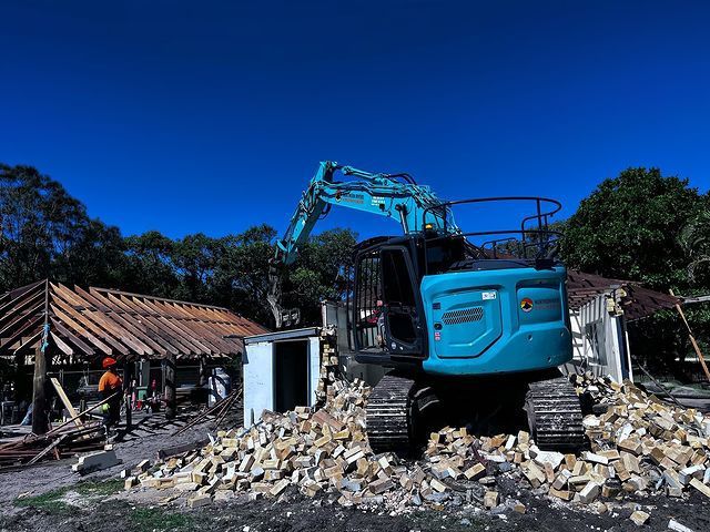 A Blue Excavator Is Demolishing a Building in A Field — Northern Rivers Demolition & Asbestos in Casino, NSW