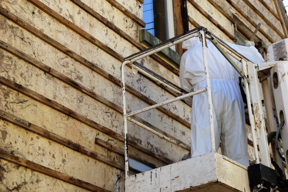 A Man in A White Suit Is Working on A Wooden Building — Northern Rivers Demolition & Asbestos in Casino, NSW