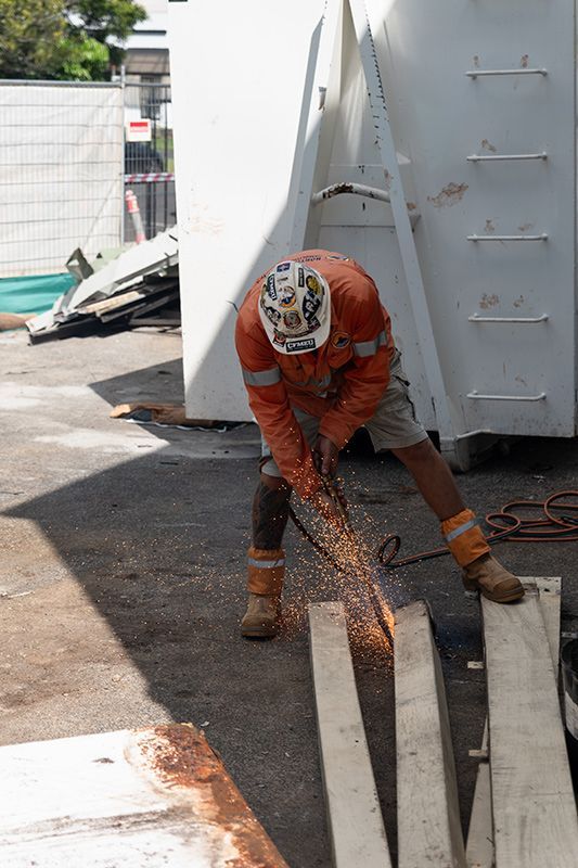 A Man Wearing a Hard Hat Is Cutting a Piece of Wood with A Saw — Northern Rivers Demolition & Asbestos in Tweed Heads, NSW