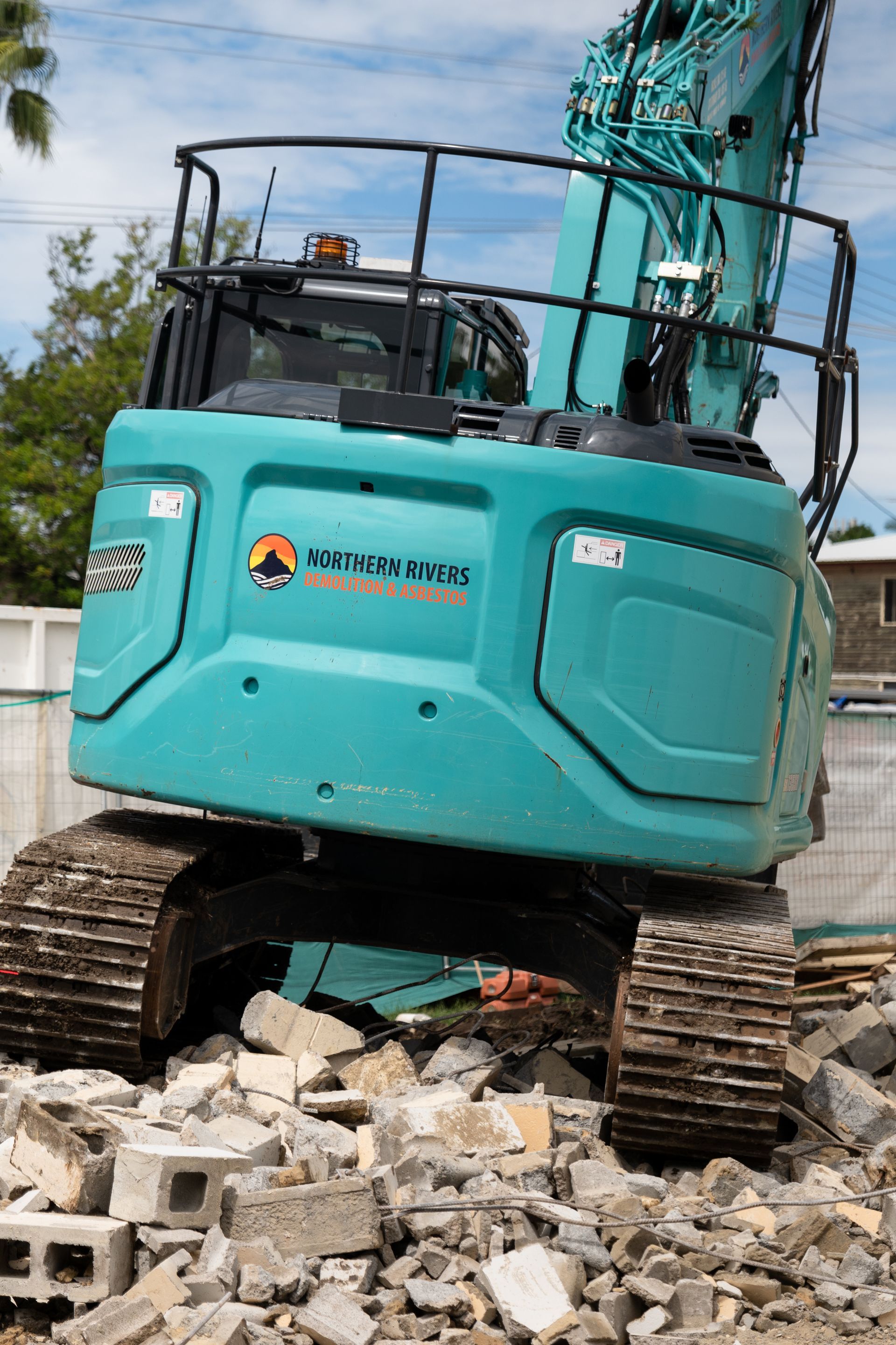 A Blue Excavator Is Working on A Dirt Field Behind a Fence — Northern Rivers Demolition & Asbestos in Skennars Head, NSW