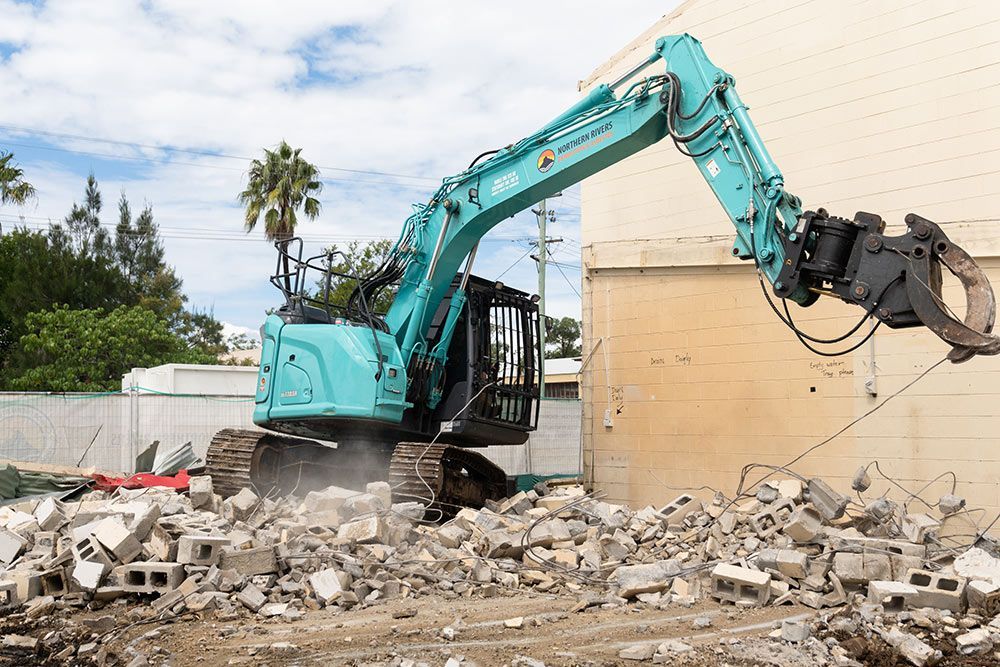 A Large Blue Excavator Is Destroying a Building — Northern Rivers Demolition & Asbestos in Grafton, NSW