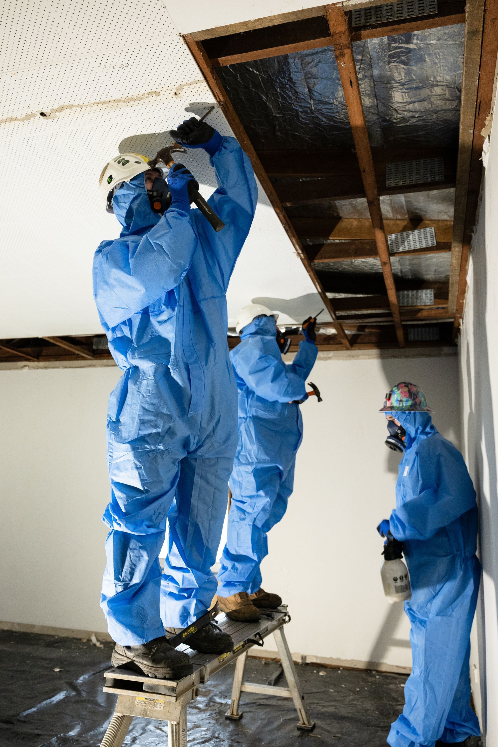 A group of people wearing blue protective suits are working on a ceiling.
