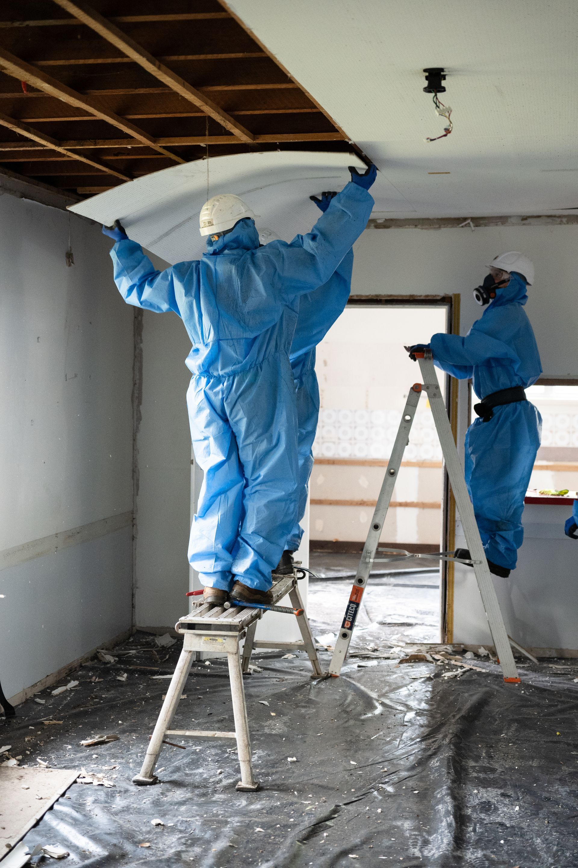 Two people in protective suits are working on a ceiling.