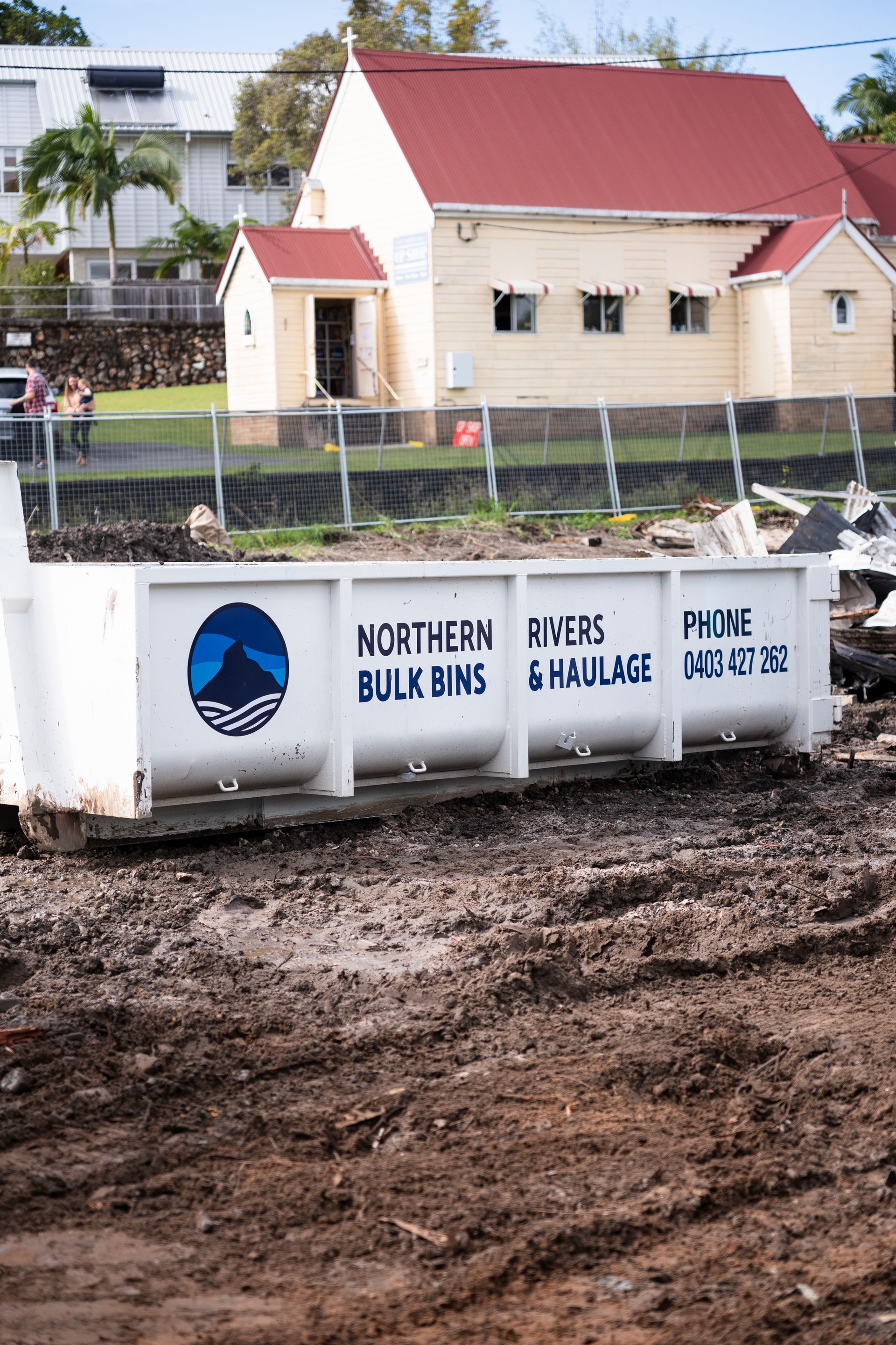 A white dumpster is sitting in the dirt in front of a house.