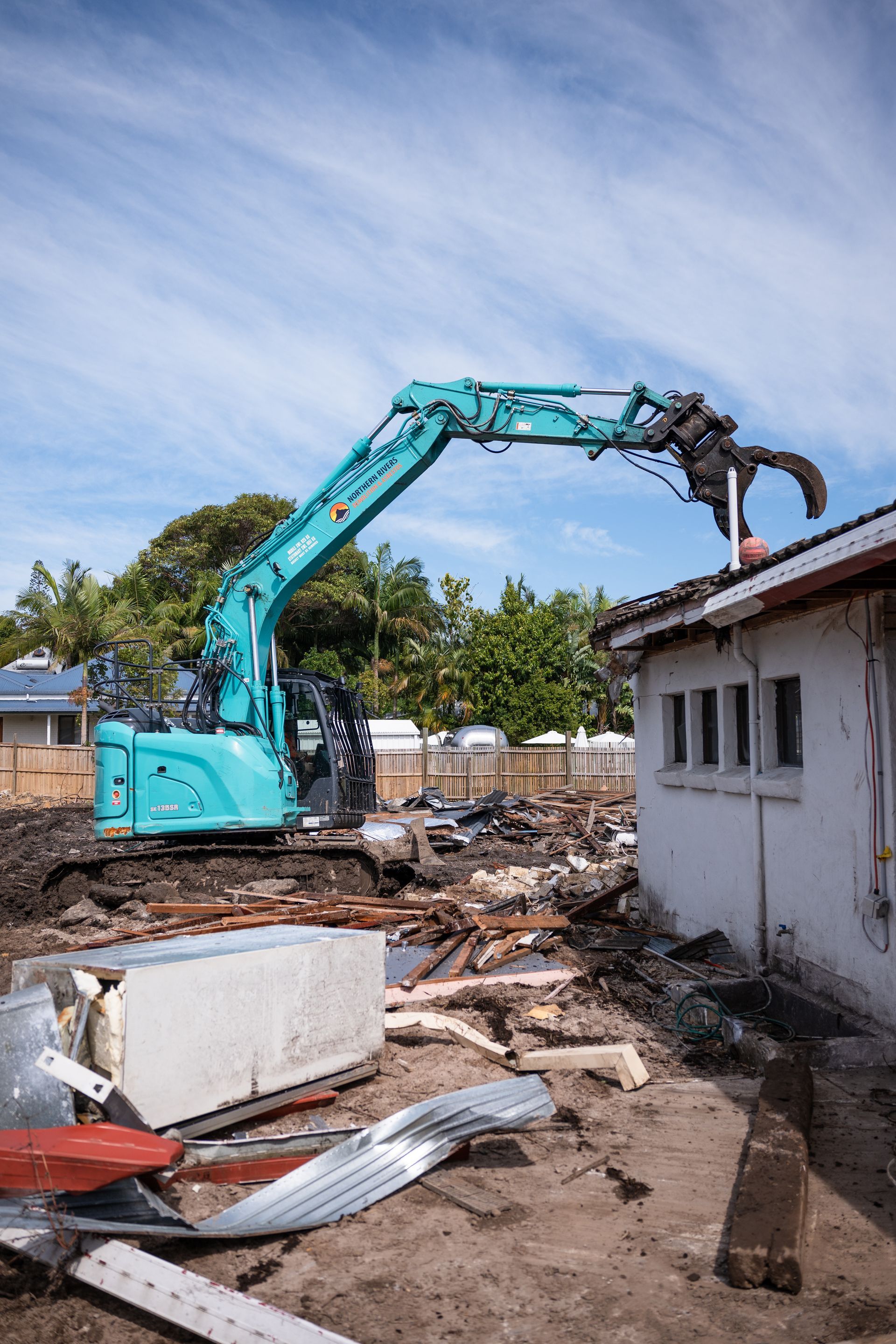 A blue excavator is demolishing a house.