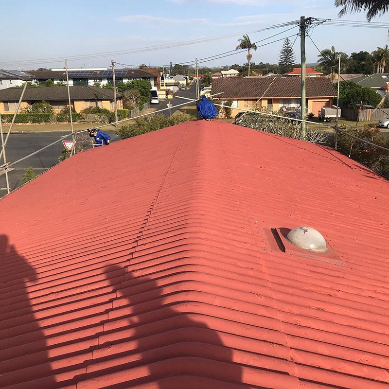 A Man Is Sitting on Top of A Red Tiled Roof — Northern Rivers Demolition & Asbestos in Grafton, NSW
