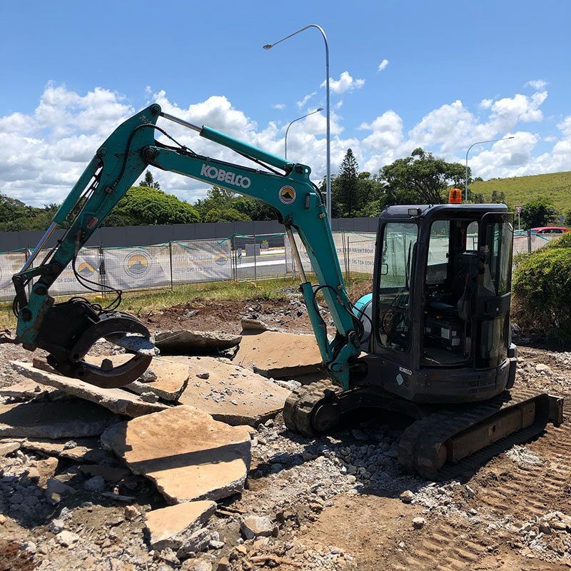 A Green Excavator Is Sitting on Top of A Pile of Rocks — Northern Rivers Demolition & Asbestos in Ballina, NSW