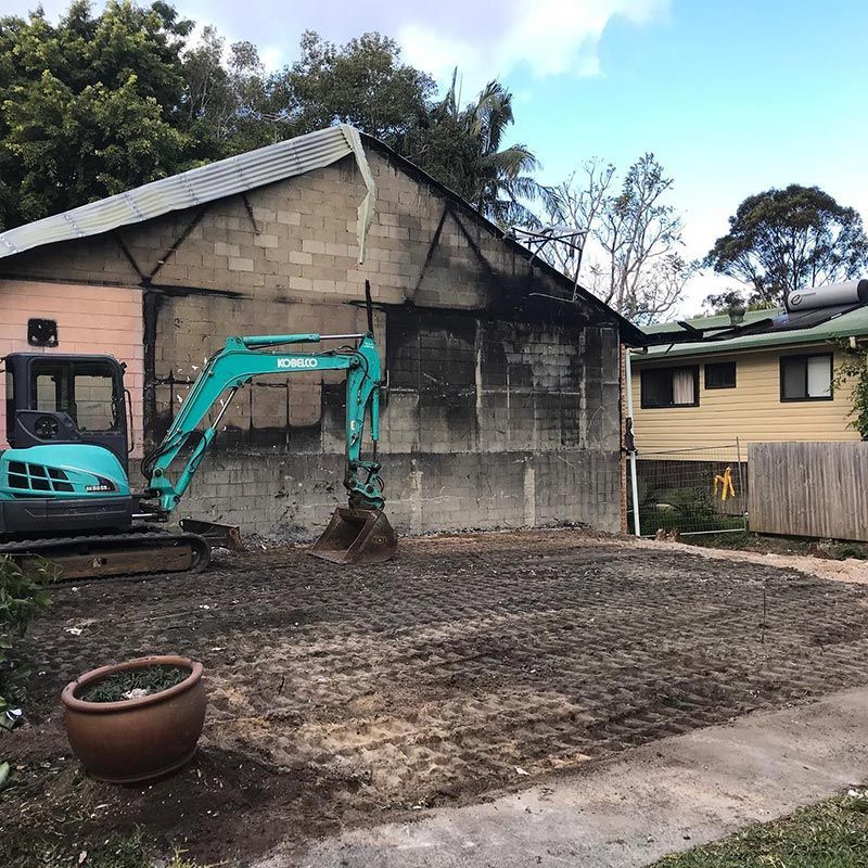 In Front of A Brick Building Sits a Blue Excavator — Northern Rivers Demolition & Asbestos in Yamba, NSW