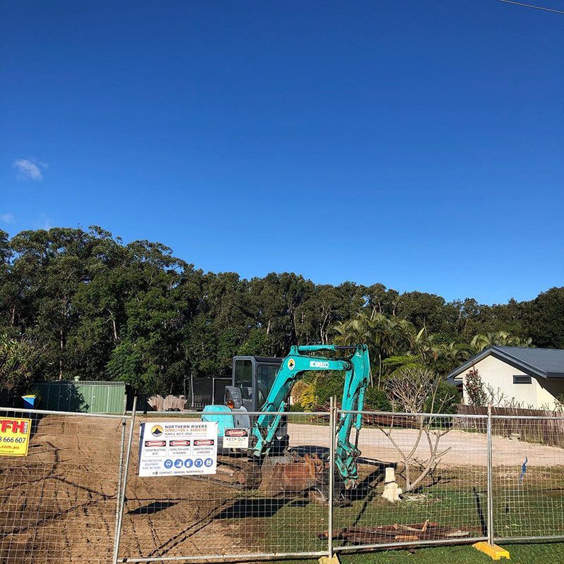 A Green Excavator Is Sitting on Top of A Dirt Field Behind a Fence — Northern Rivers Demolition & Asbestos in Byron Bay, NSW